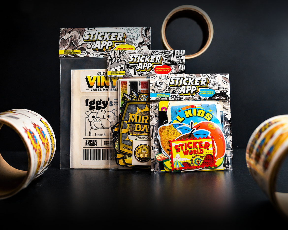 StickerApp sample packs featuring vinyl, holographic, and die-cut sticker examples displayed in branded packaging with sticker rolls in the background.