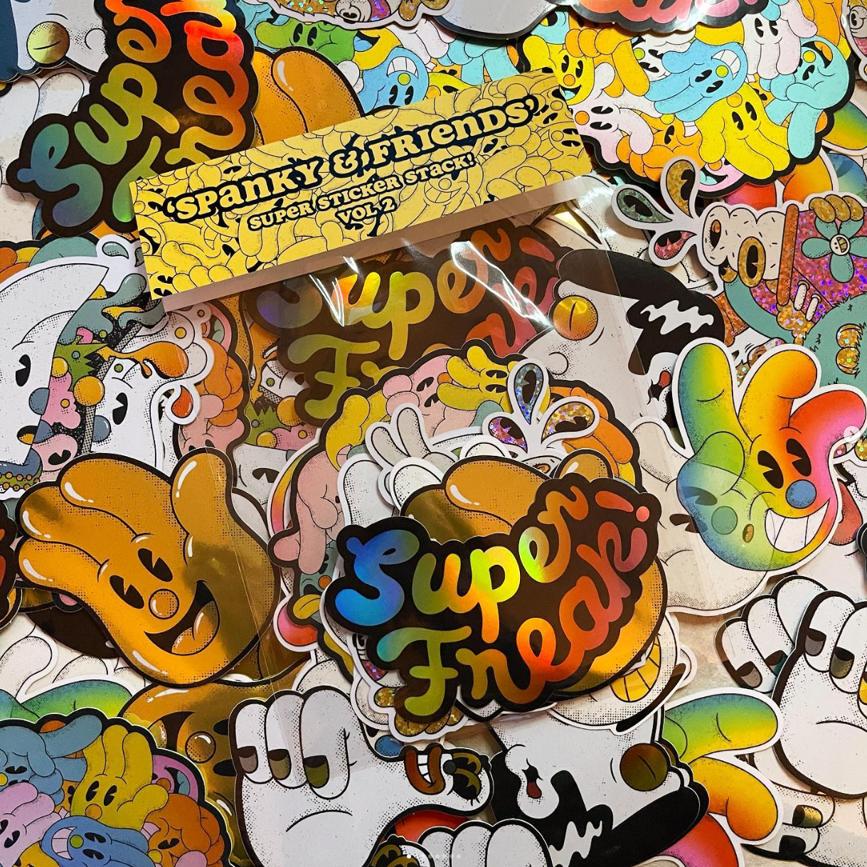 A colorful assortment of die-cut stickers featuring playful cartoon hands and characters, with a label reading "Spanky & Friends Super Sticker Stack Vol. 2."
