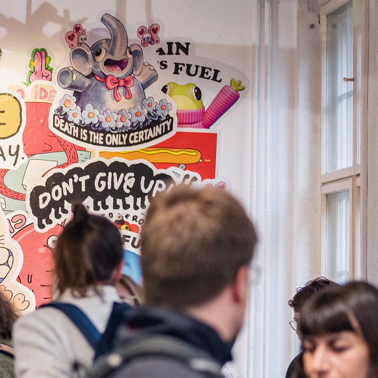 Visitors at an art exhibition talking, behind them artwork made of wall stickers hanging on display.
