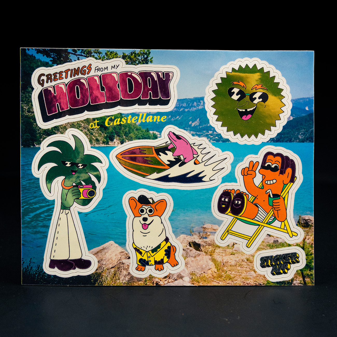 Colorful sticker sheet placed on a scenic postcard-style background with a lake and mountains. Features playful cartoon characters including a palm tree with a camera, a smiling dog, a sun-like face, and a character relaxing in a chair, along with the text “Greetings from my holiday at Castellane.”