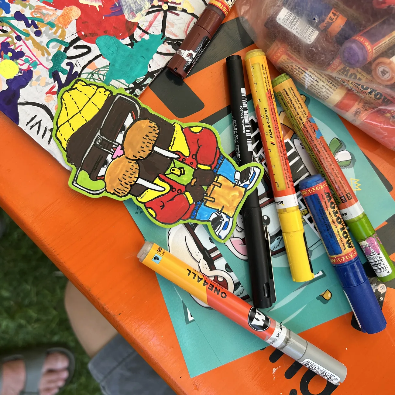 Hand-coloured Brainfart die-cut sticker of a character in a yellow beanie and red jacket, surrounded by paint markers