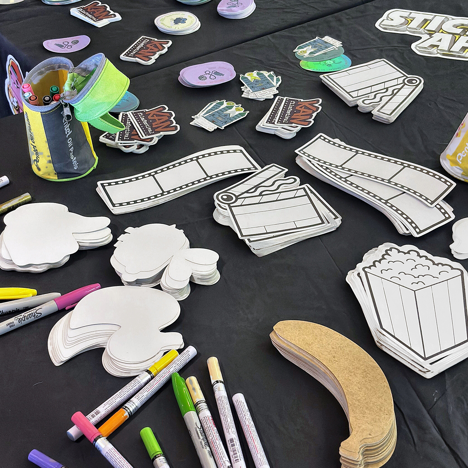 Sticker-making table at KAN filmfestival with blank die-cut stickers shaped like popcorn, film strips and clapperboards, kraft paper stickers and paint markers