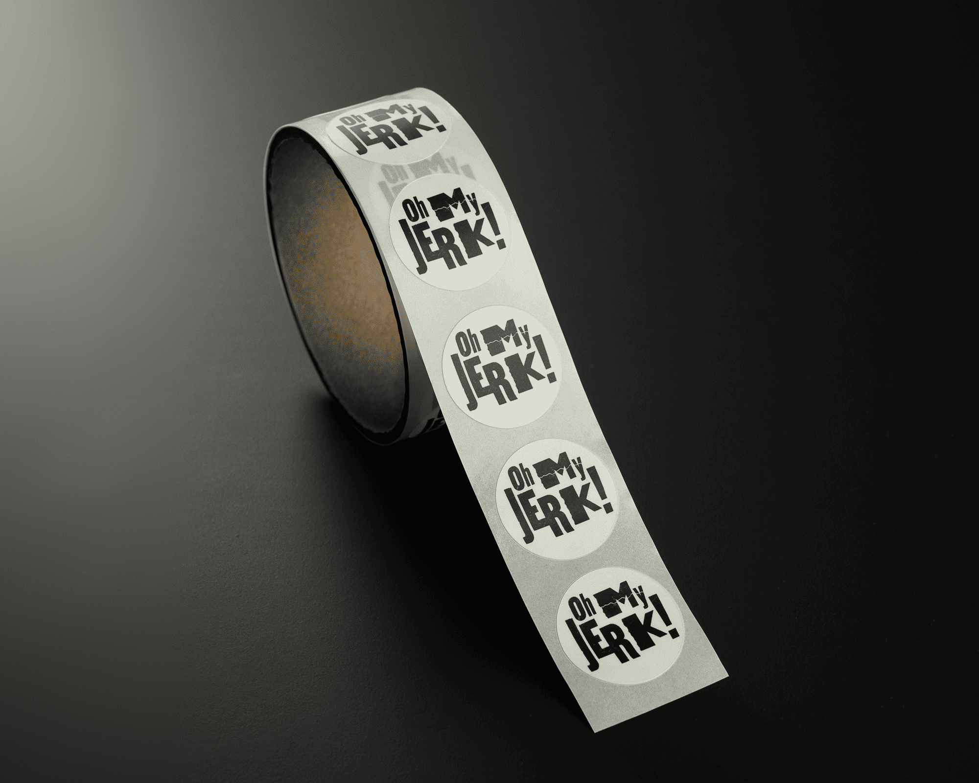 A roll of labels on a dark surface, each featuring the bold text "Oh My Jerk!" in black and white.