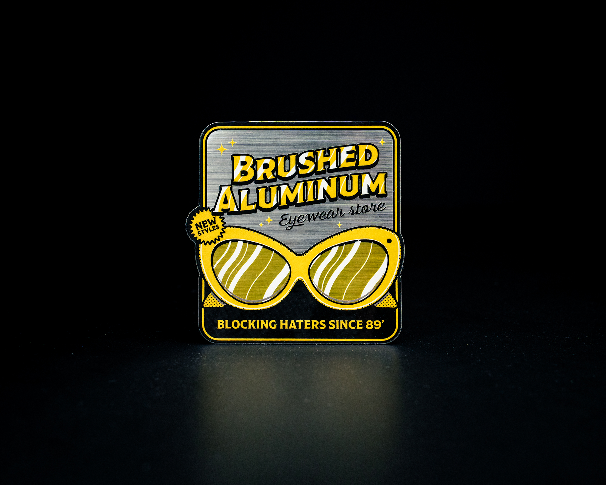 Retro-style sticker for "Brushed Aluminum Eyewear Store" featuring yellow sunglasses and the tagline "Blocking Haters Since 89'."