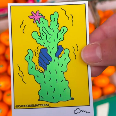 Bright illustration of a whimsical green cactus with blue and pink accents, set against a yellow background, created by @capucinemattiussi_.