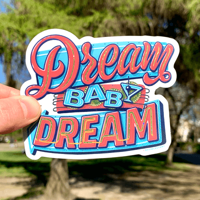 Dream baby dream vinyl sticker held in hand against trees in the background.