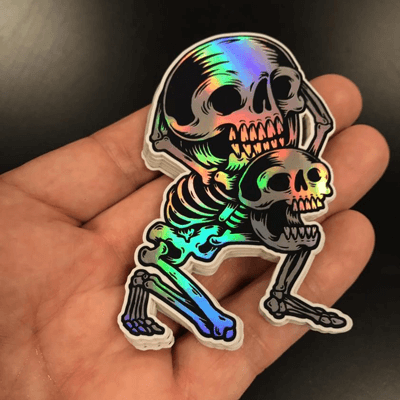 Hand holding pile of holographic stickers of skulls.