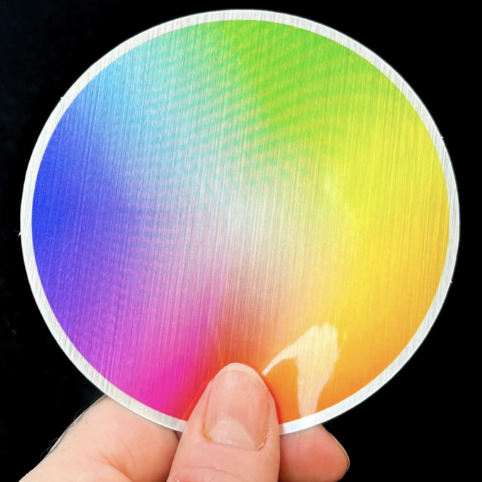 A hand holding a brushed aluminum rainbow colored sticker